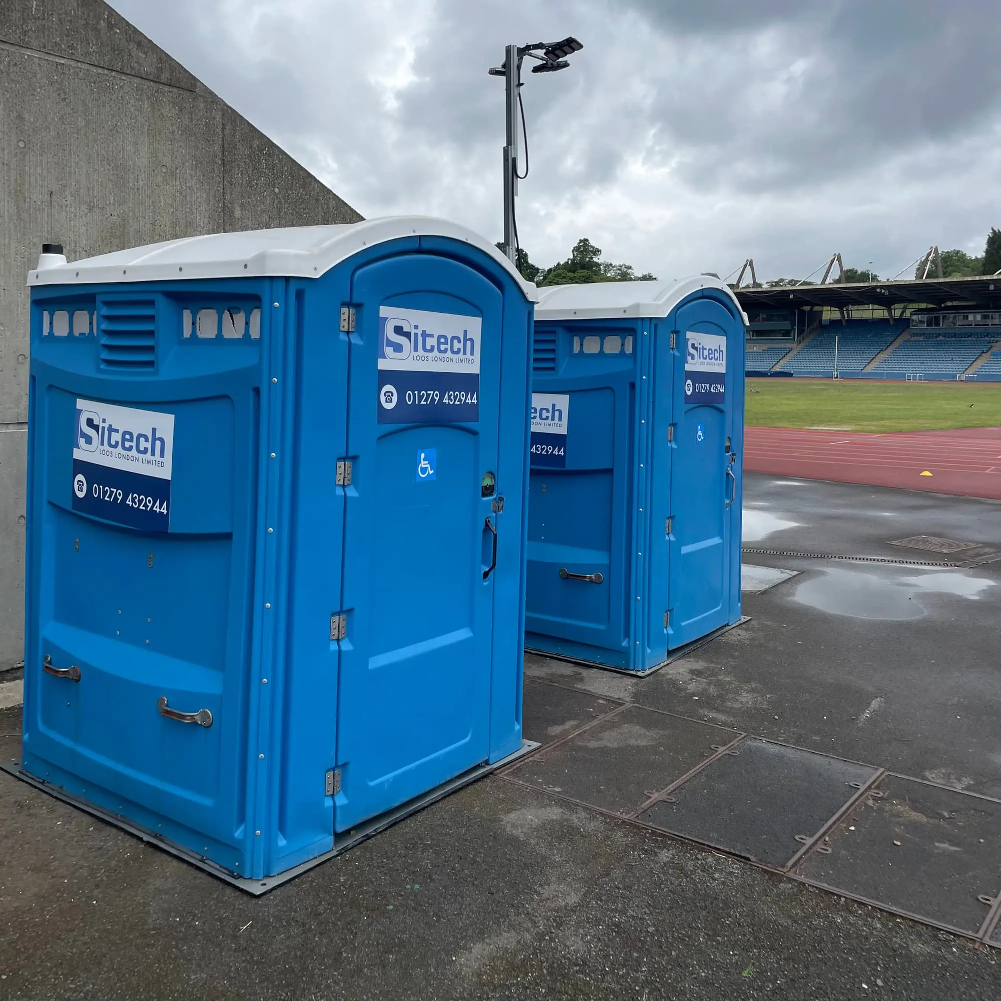 Two Sitech Loos London disabled access portable toilets with wheelchair symbols on the doors, sited on firm hard-standing beside an athletics stadium
